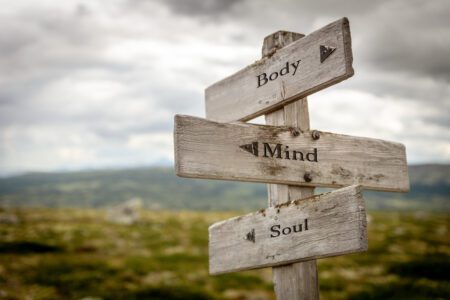 Weathered, wooden stacked sign posts with typed words “Body”, “Mind”, and “Soul”, in front of…
